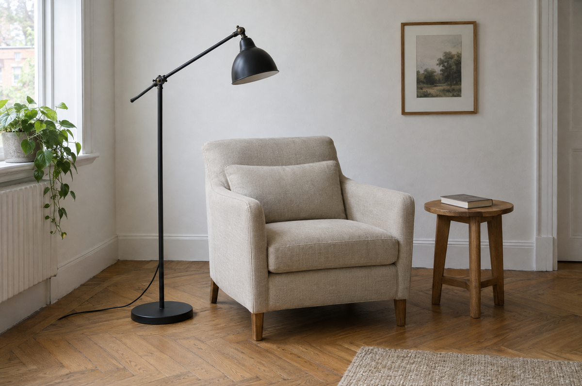 Lampadaire en métal noir mat à bras orientable à côté d'un fauteuil en lin, sur un parquet en chevron